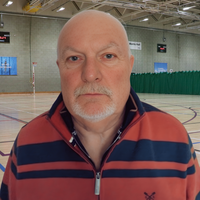 Headshot of John. Older man in stripey quarter zip looking at camera.
