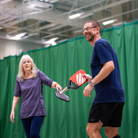 Man and woman tapping pickleball rackets.