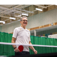 Older man smiling and playing table tennis.