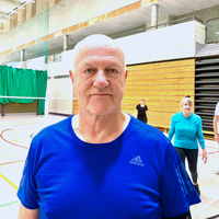 Headshot of Howard, a man in his 50s wearing a blue t-shirt looking at camera in a sports hall.