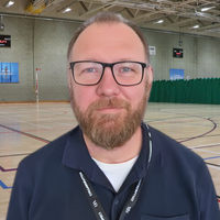 Headshot of Alex. Man in 40s in glasses smiling at camera.