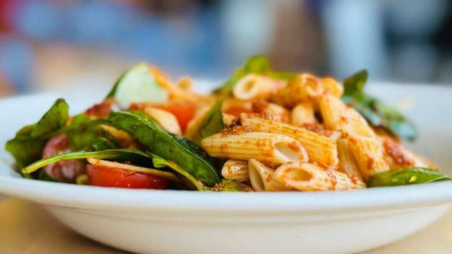 A plate of penne pasta with spinach, cherry tomatoes, and a light sauce, garnished with herbs, served on a white dish.