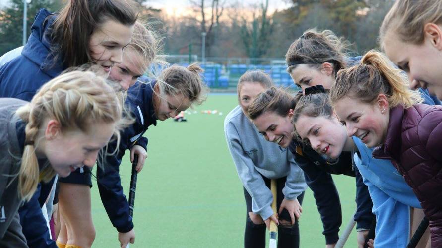 Women playing hockey gathered in circle,