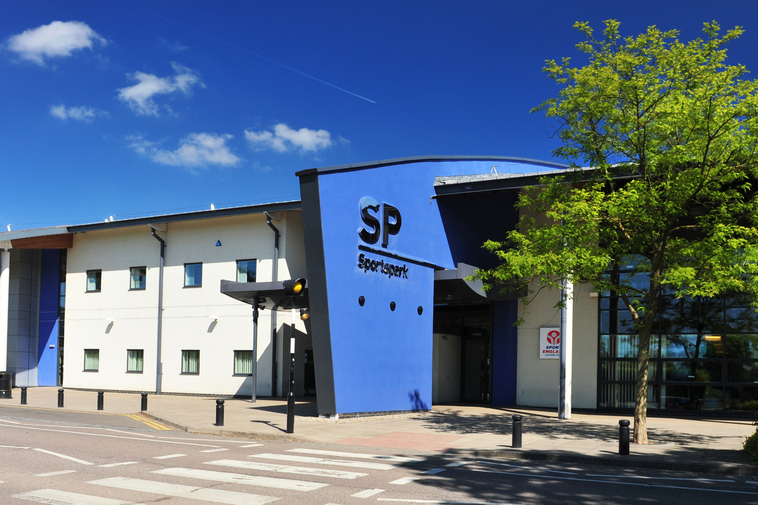 Sports centre entrance from across the street. Blue building with tree in front.