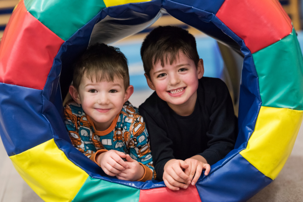 Two boys laying down in soft play gymnastics tub smiling at camera.