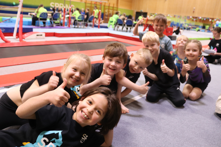 A group of children smiling and giving thumbs up to the camera in a gymnastics centre.