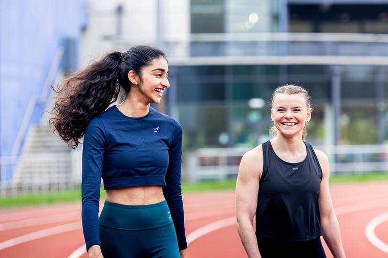 Two girls smiling walking side by side on athletics track