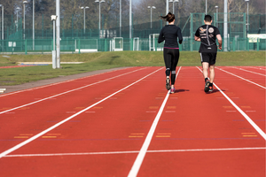 man and woman jogging on athletics track away from camera