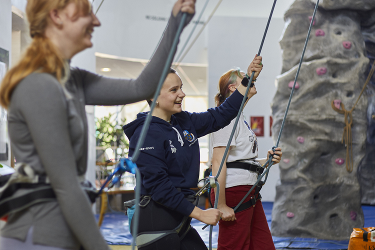 three girls with climbing ropes in front of climbing wall