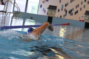 Man swimming front crawl in indoor swimming pool away from camera.