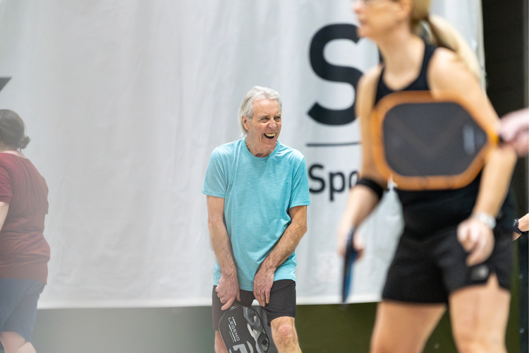 Older man smiling playing pickleball in group.