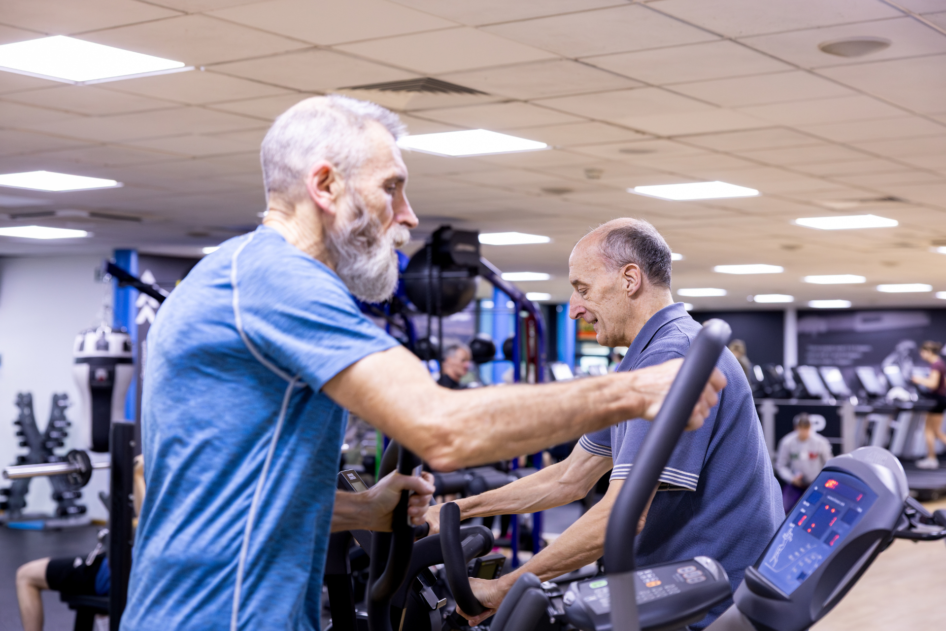 Two older men on cardio machines in gym
