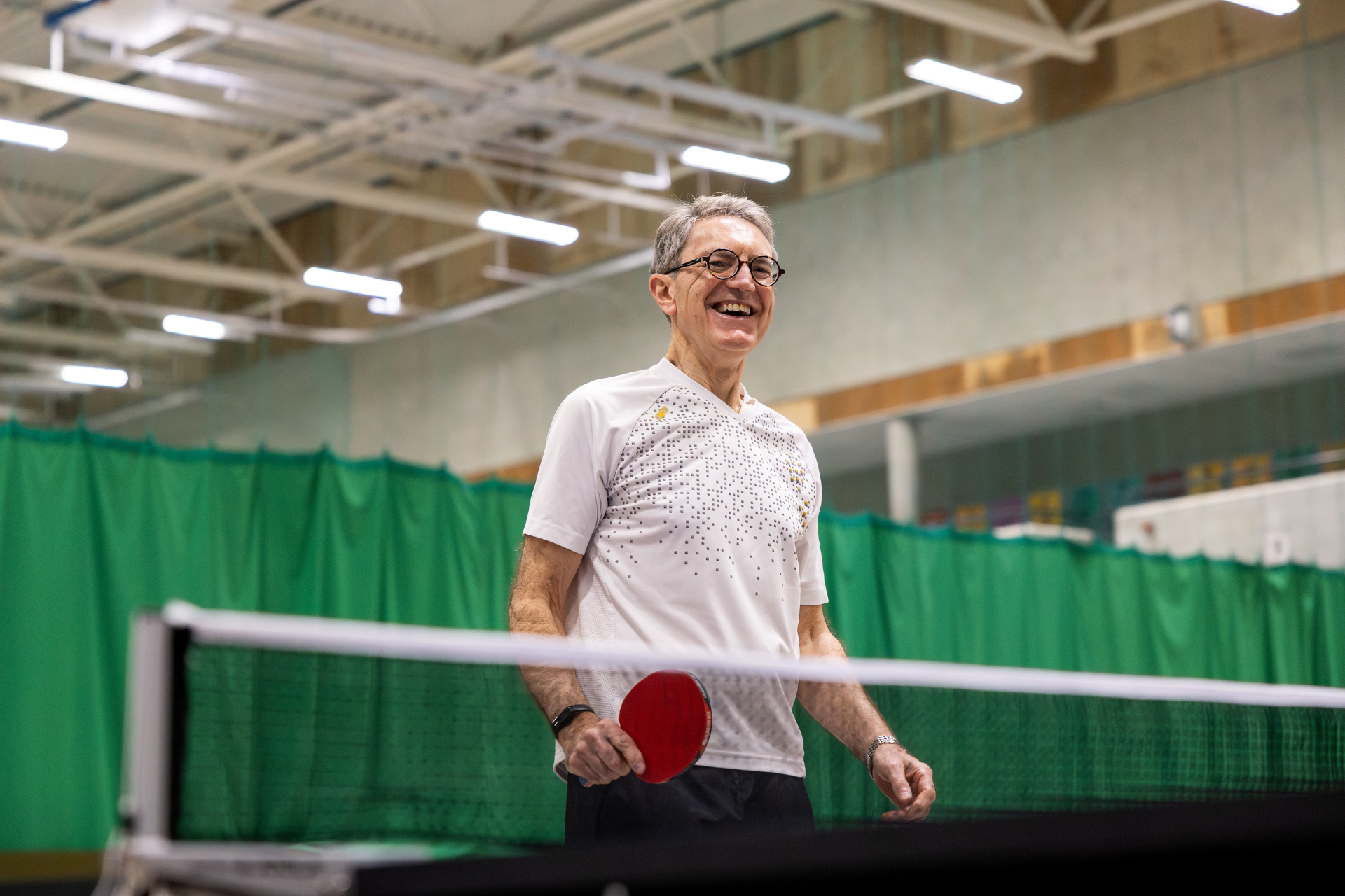 Older man smiling and playing table tennis.