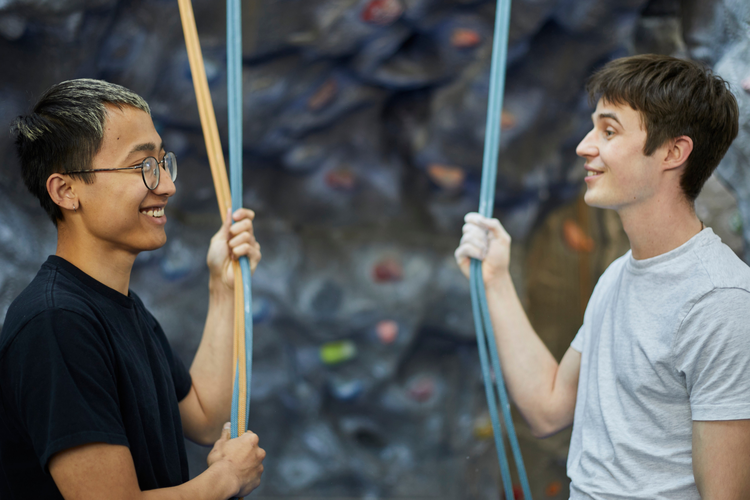 Two men at climbing wall smiling at each other.