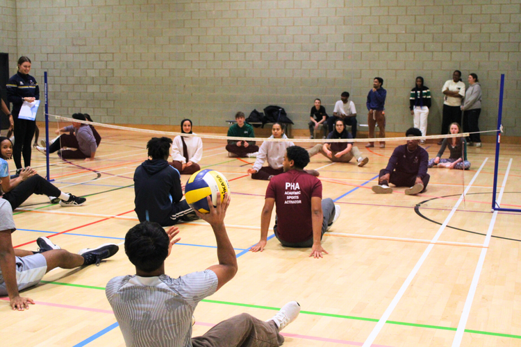 Two teams playing sit down volleyball in sports hall.