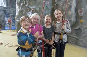 three girls one boy at climbing wall birthday party smiling at camera