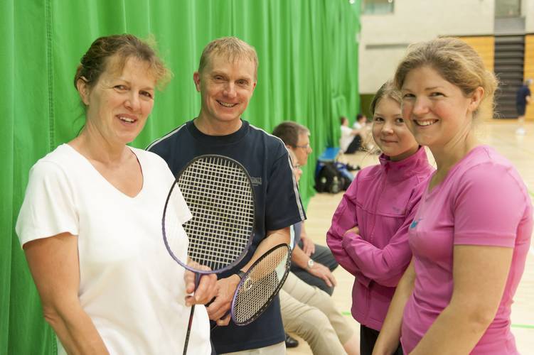three women and one man smiling at camera holding badminton rackets