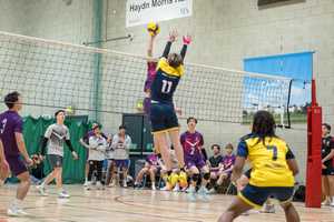 UEA and Loughborough university play men volleyball. Two players jump for ball at net.