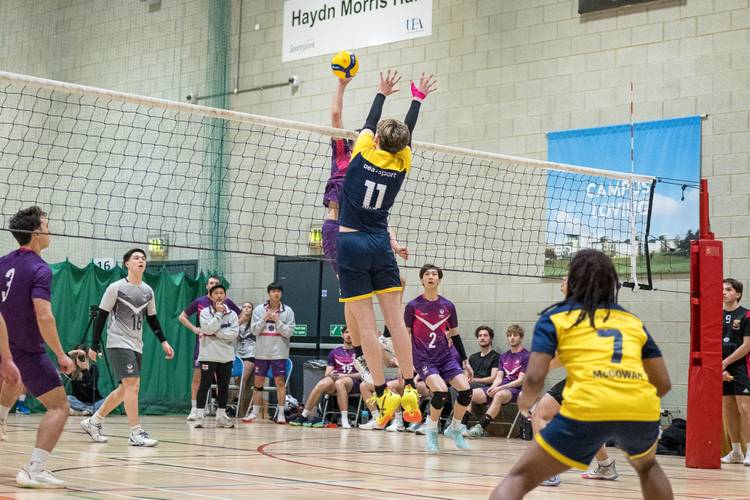 UEA and Loughborough university play men volleyball. Two players jump for ball at net.