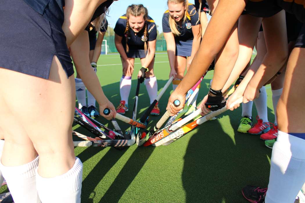 Group of girls in circle holding out their hockey sticks so they touch in the middle of circle.