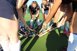 Group of girls in circle holding out their hockey sticks so they touch in the middle of circle.