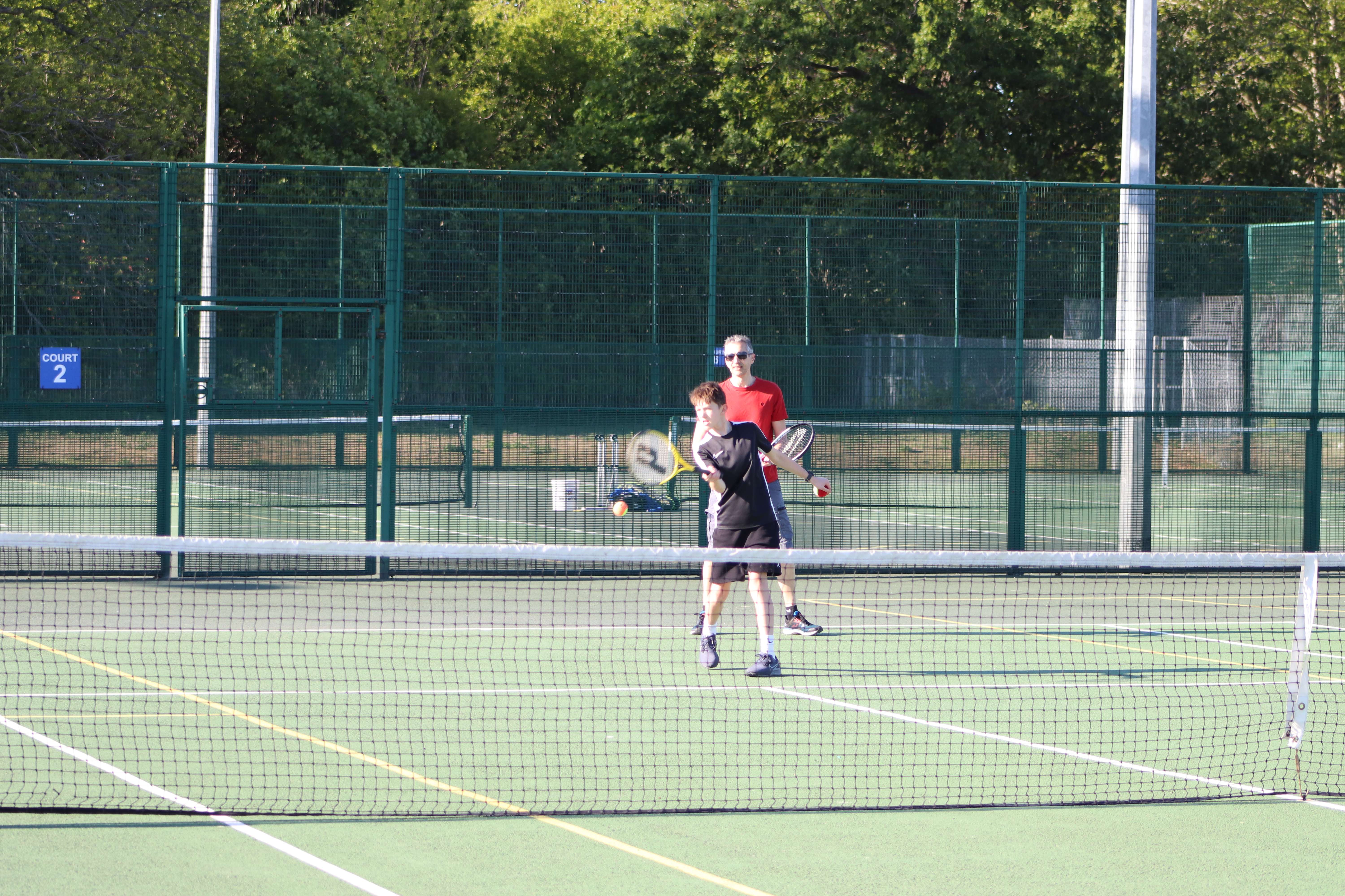 father and sun playing tennis outside on sunny day
