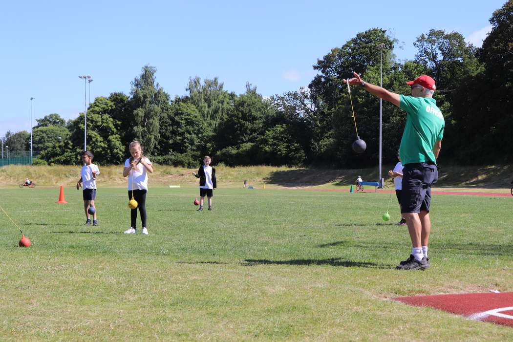 Man teaching children how to hammer throw outside.