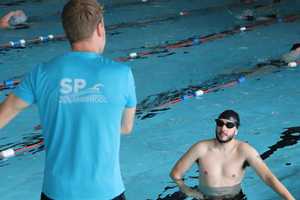Swimming teacher speaking to male student in pool.