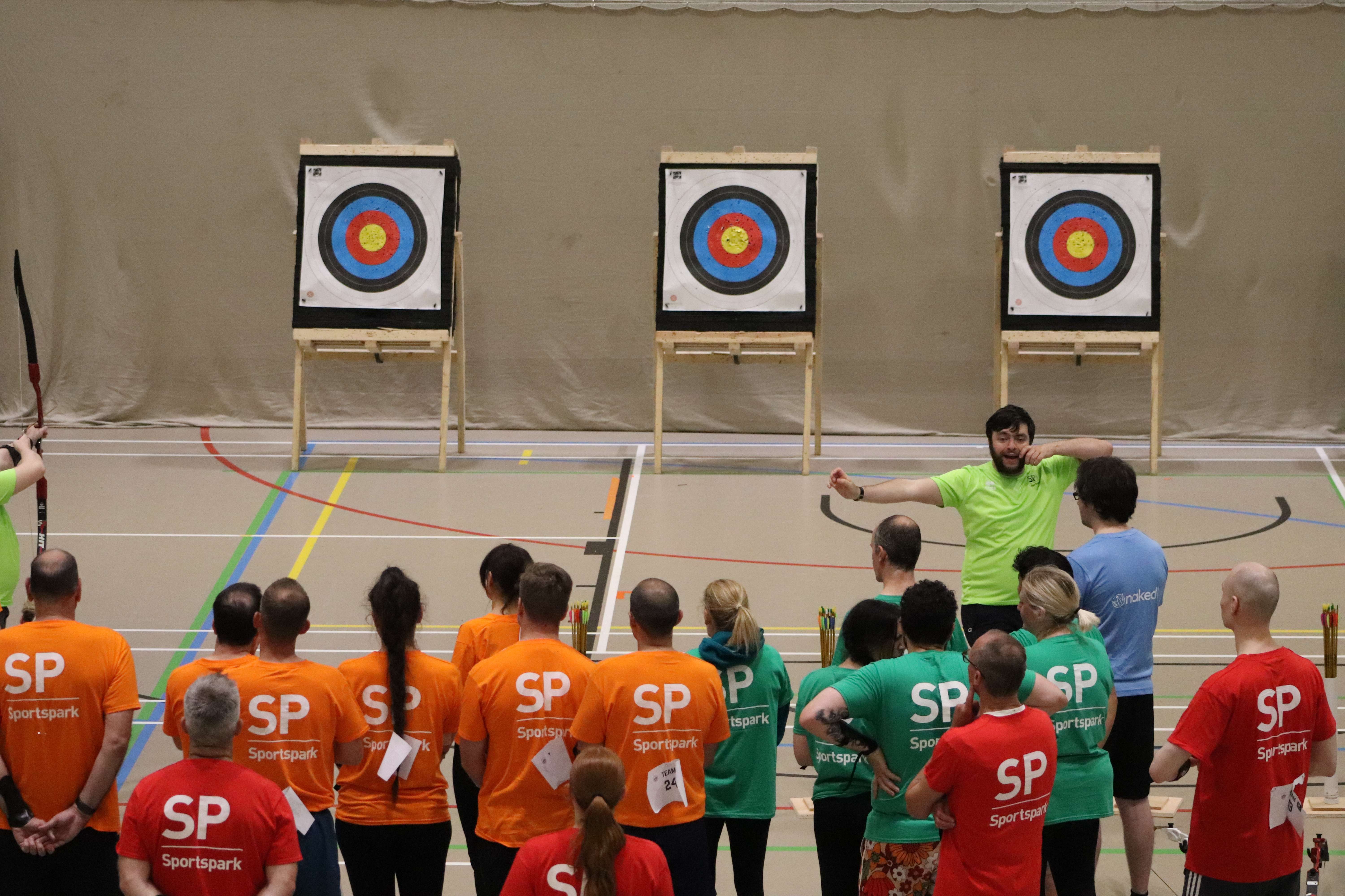 archery instructor teaching large group of people archery in front of targets.
