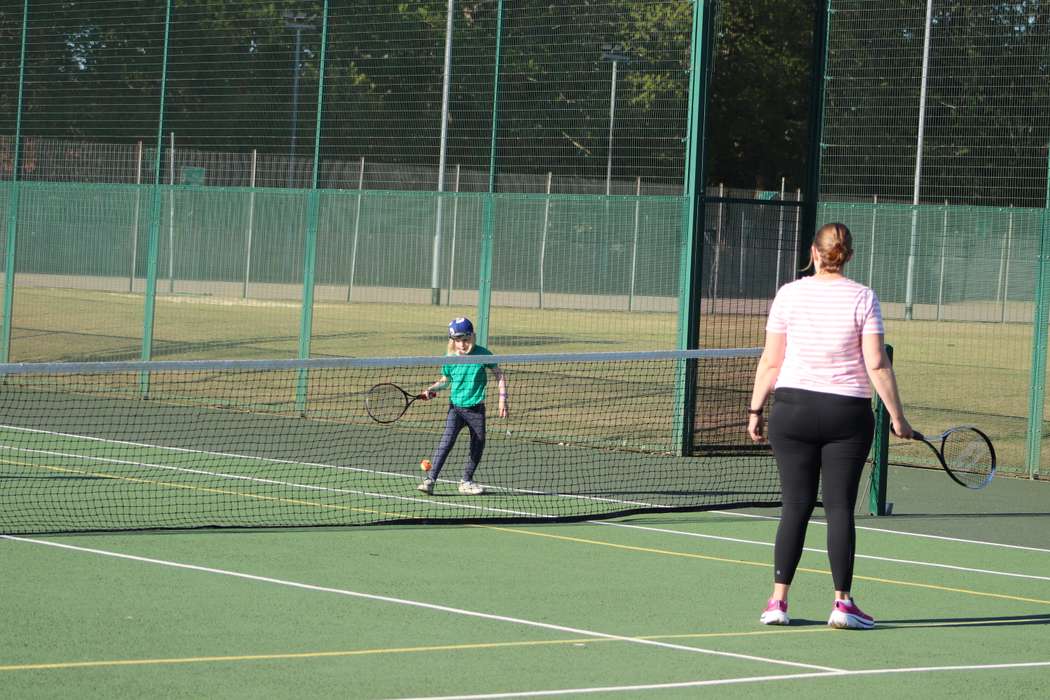 mother and son playing tennis outside on sunny day.