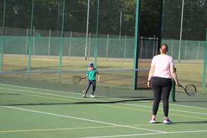 mother and son playing tennis outside on sunny day.