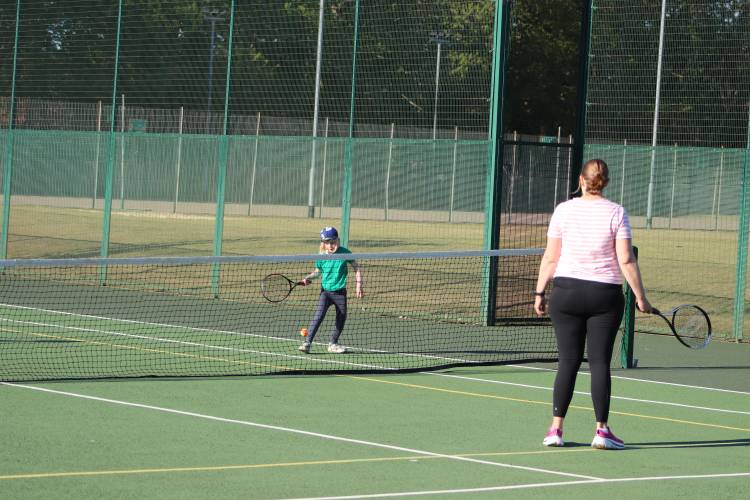 mother and son playing tennis outside on sunny day.