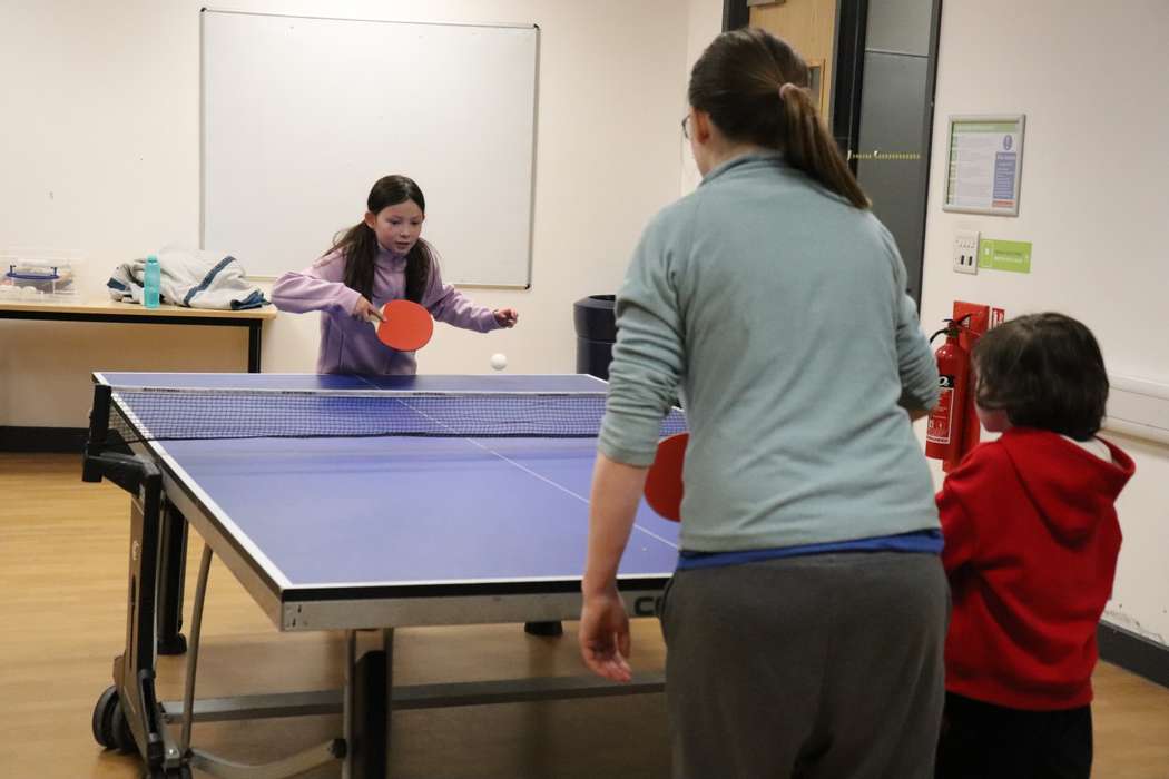 Mother and two children playing table tennis indoors.