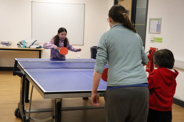 Mother and two children playing table tennis indoors.