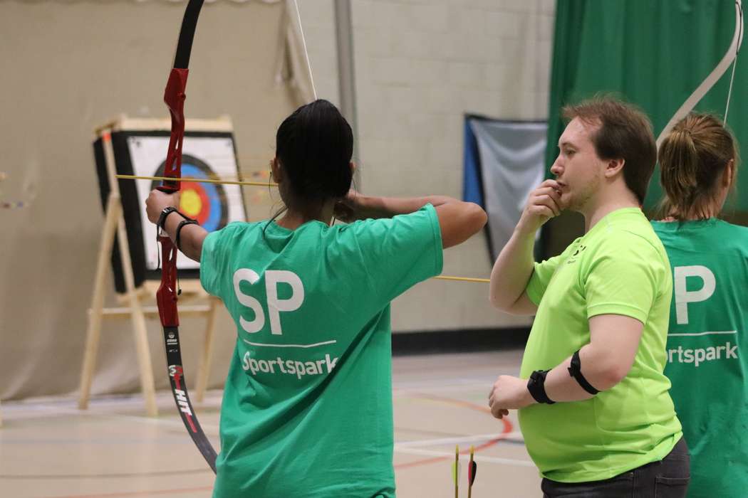 instructor teaching girl archery in sports hall