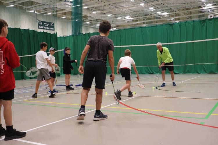 Three children lining up to play badminton with Sportspark coach.