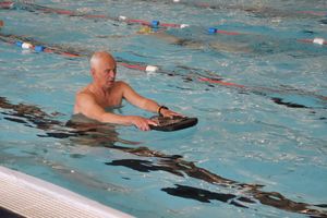 Older man swimming with floating aid in pool.