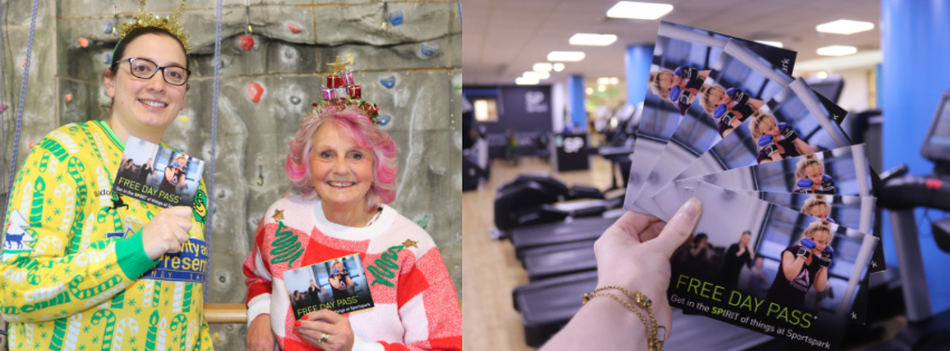 Two ladies in Christmas jumpers holding day passes in front of climbing wall.