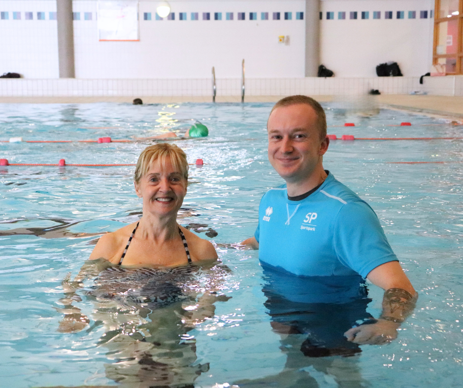 Male swim instructor and older lady standing in pool smiling at camera.